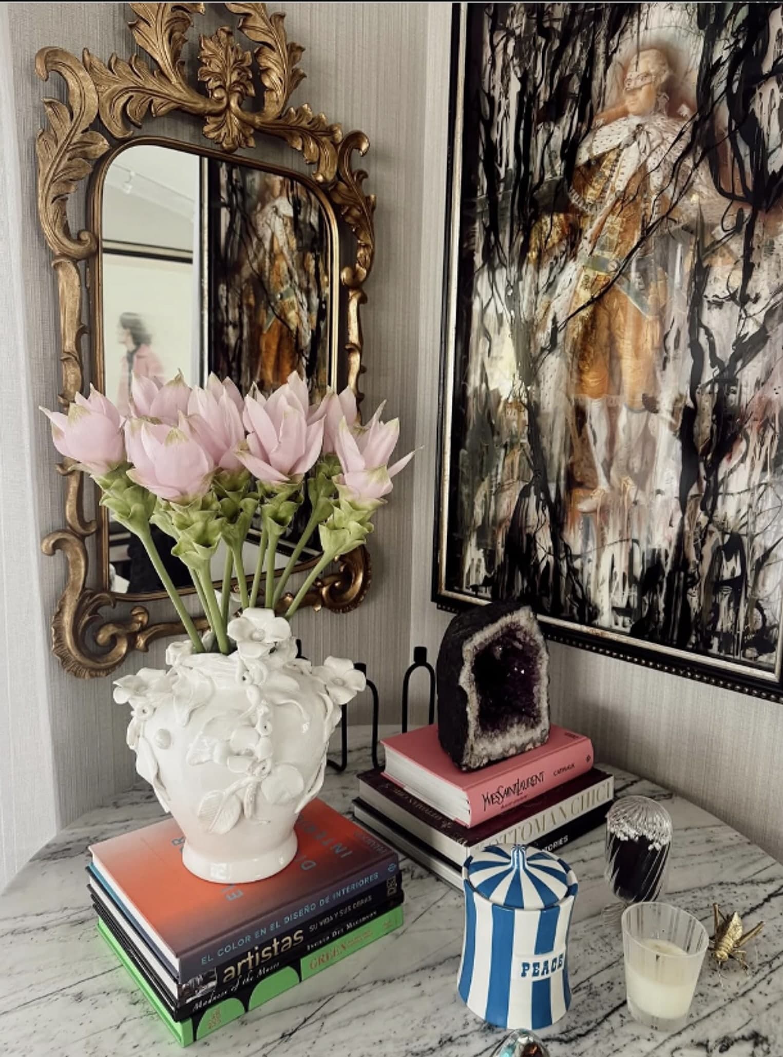 Una mesa con espejo dorado, proteas rosadas y arte enmarcado en un interior cálido y habitado.